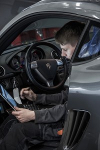 Bild på mekaniker på Porsche Service Center Haninge med handdator i knät sittande i en Porsche.